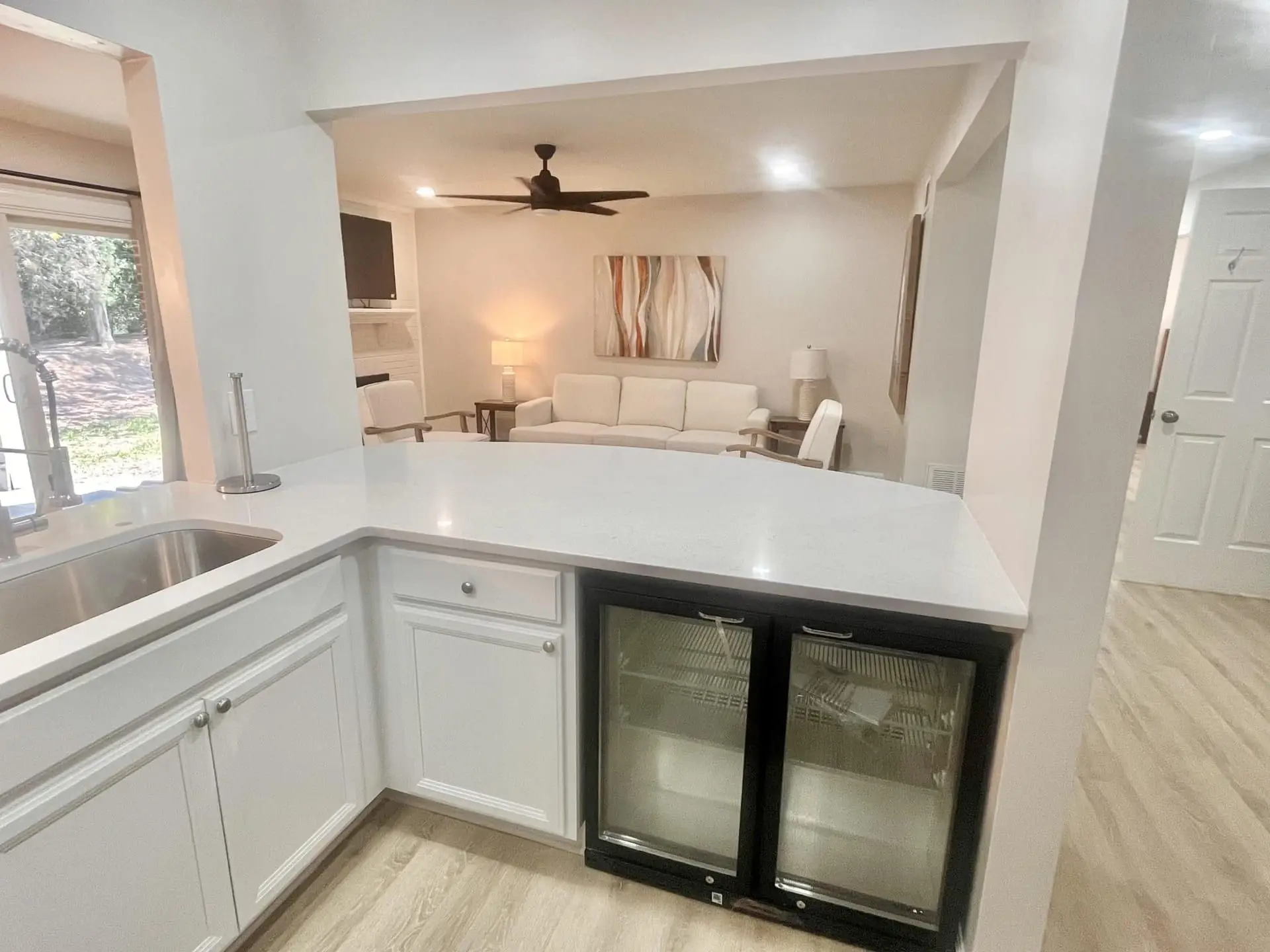 Kitchen peninsula in quartz with a double sink and beverage coolers, open to the living room