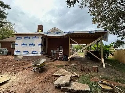 Brick house mid-build: new carport framing up and the walls wrapped in housewrap